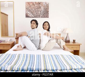 Young man woman sitting back to back on bed MR#702V,702U Stock Photo