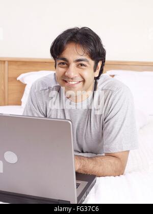 Young man with laptop laying on bed MR#702V Stock Photo