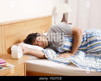 Young man sleeping lying on bed hand stopping ringing alarm clock MR#702V Stock Photo