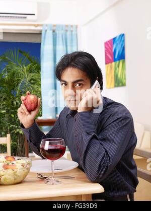 Young man listening on mobile holding red apple in one hand MR#702V Stock Photo