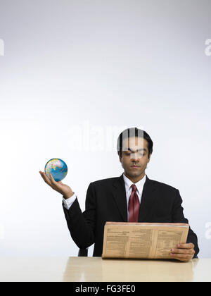 Businessman holding globe in hand and reading newspaper MR Stock Photo