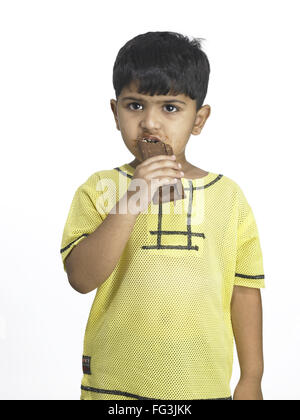 South Asian Indian boy eating chocolate in nursery school MR Stock Photo