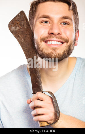 Young man with shaving having fun with machete large knife. Handsome guy removing face beard hair. Skin care and hygiene humor. Stock Photo