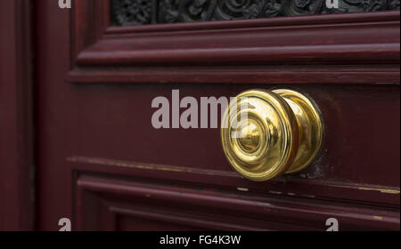 Shiny brass metal doorknob on maroon red wooden entrance door Stock Photo