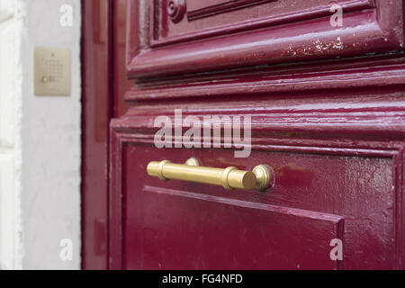 Old brass door handle on sturdy old textured maroon red wooden door Stock Photo