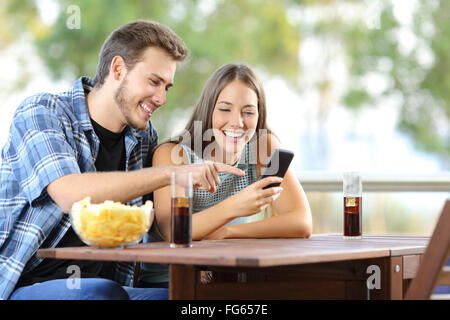 Couple sharing a smart phone sitting on a hotel or home terrace Stock Photo