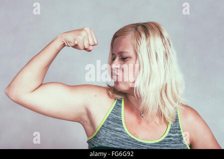 Strong confident muscular woman flexing her muscles. Young blond sporty female showing arm and biceps. Stock Photo