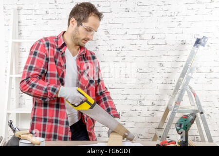 a smiling young man cutting a board with a hand saw Stock Photo
