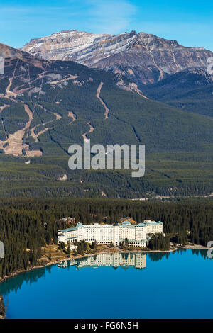 Chateau Lake Louise reflected in the tranquil intense blue mountain lake with ski hill runs in the background and blue sky Stock Photo