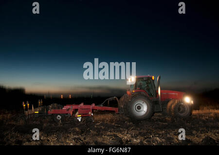 Agriculture - A Tractor Pulling A Disk Ripper At Dusk Tills A Field Of Corn Stalks And Residue After The Harvest, Preparing The Field For The Winte... Stock Photo