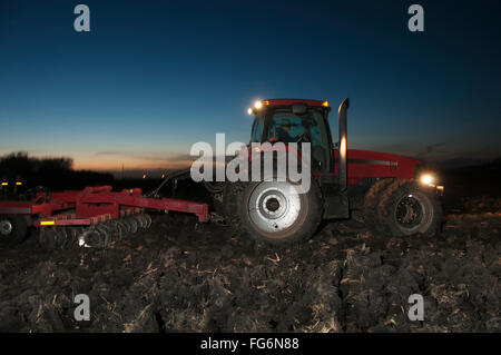 Agriculture - A Tractor Pulling A Disk Ripper At Dusk Tills A Field Of Corn Stalks And Residue After The Harvest, Preparing The Field For The Winte... Stock Photo