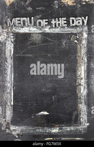 Blackboard in grunge style, scratched and ruined, with message 'Menu of the day'. Stock Photo