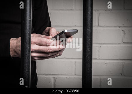 A prisoner in prison using a mobile phone behind bars in a cell Stock Photo