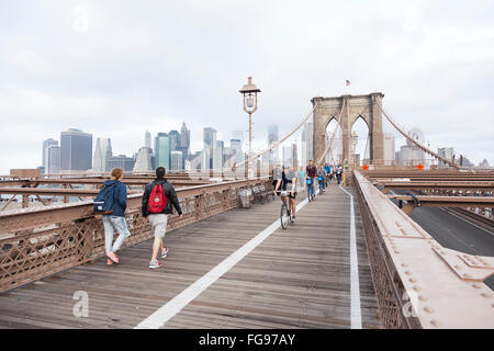 people engaged in bike run and others walking on brooklyn bridge new york with manhattan in the background Stock Photo