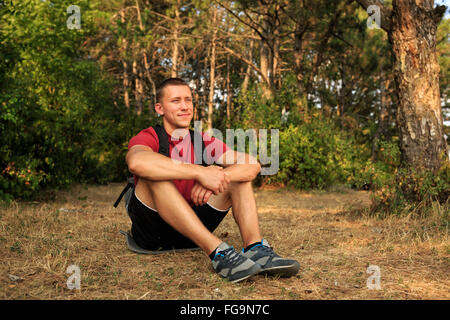 Happy hiker man sitting on the ground and looking forward Stock Photo