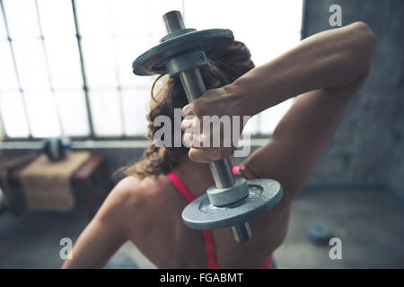 Body and mind workout in loft fitness studio. Seen from behind fitness woman lifting dumbbell Stock Photo