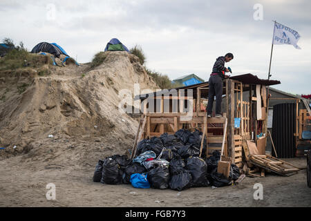 A Syrian man builds his family shelter next to a sand dune in the Jungle refugee camp, Calais, France. Stock Photo