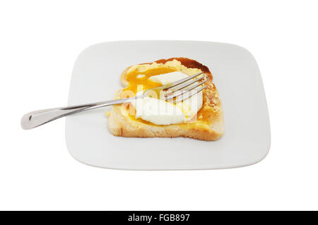 Runny yolk poached egg on toast with a fork on a plate isolated against white Stock Photo