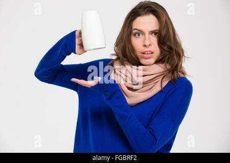 Confused lovely young woman holding empty inverted mug over white background Stock Photo