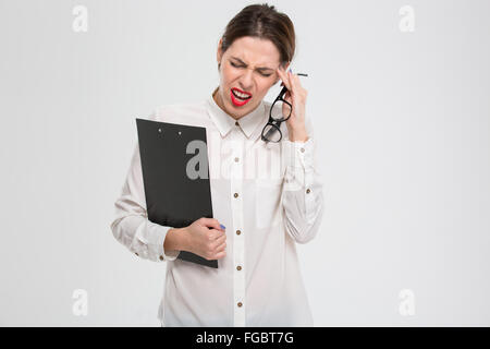 Depressed unhappy young business woman with clipboard and glasses suffering from headache over white background Stock Photo