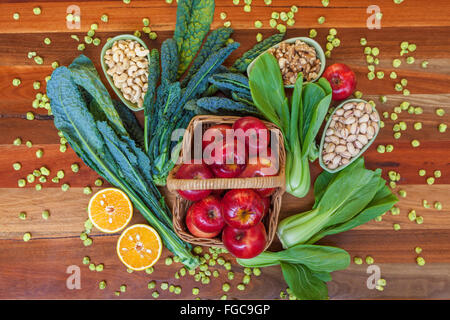 Health food composition with apples in basket, green leafs, and nuts placed on wooden table. Top view. Stock Photo