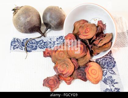 Thin round beetroot chips baked in the oven with oregano,salt poured out of a bowl and ripe beet roots on a kitchen towel isolat Stock Photo