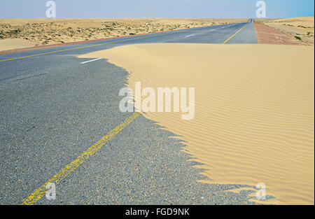 Wind has blown sand from dunes onto the highway that crosses Wahiba Sands desert in Oman. Stock Photo
