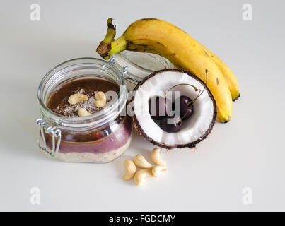 Cherry coconut banana overnight oats with cracked open coco, banana, cashews mixed with chia seeds and cherry cream in a mason j Stock Photo