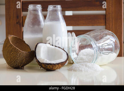 Coconut products. Cracked open coconut with meat cut in half, grounded flakes in a mason jar, flour and fresh milk in glass bott Stock Photo