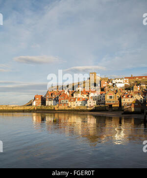 View over Whitby harbour during golden hour. Looking towards old town, church and Whitby abbey showing sea and reflections. Stock Photo