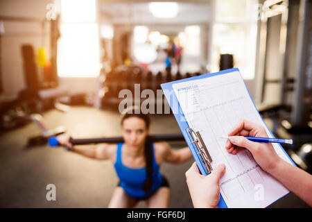 Woman exercising in gym, personal trainer, plan on clipboard Stock Photo