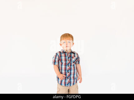 Young boy with blonde hair standing against a white background pointing his finger Stock Photo