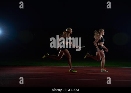 athletic runners passing baton in relay race Stock Photo