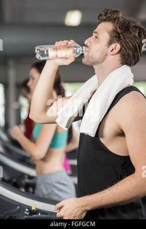 Athletic man drinking water while running on treadmill Stock Photo