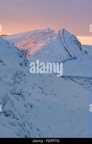 Winter on Hadrian's Wall, with the setting sun casting a pale orange glow across the snow  covered landscape Stock Photo