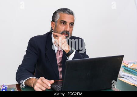 Businessman in suit and tie, concentrated, in his studio. Alone in his office, in front of the desk with the computer, it pensiv Stock Photo