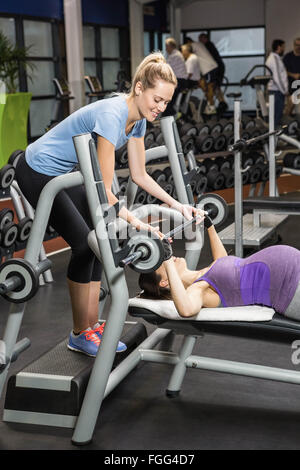 Smiling trainer helping pregnant woman lifting barbell Stock Photo