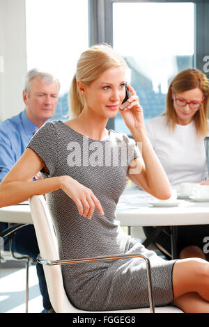 Portrait of middle age business woman sitting at meeting while making a call. Business team Stock Photo