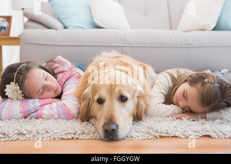 Sisters napping on rug with golden retriever Stock Photo