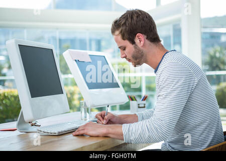 Handsome man working on computer and taking notes Stock Photo