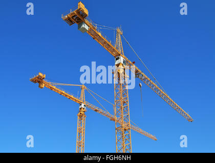 Two construction cranes against blue sky. Stock Photo