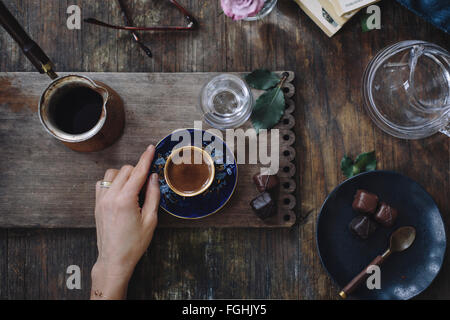 A woman is holding a cup of Turkish coffee (with foam on top) served with water and chocolate. Photographed from the top. Stock Photo