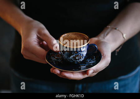 A woman is holding a cup of Turkish coffee with foam on top (with both hands). Photographed from the front. Stock Photo