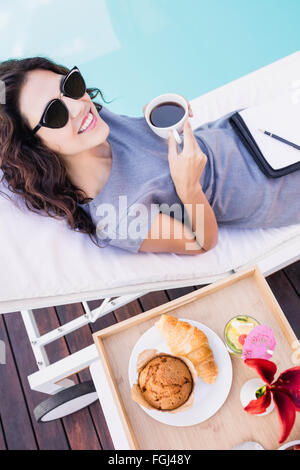 Young woman having cup of tea near poolside