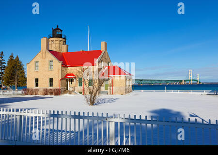 Old Mackinac Point Lighthouse in Mackinaw city sits in a blanket of snow in Mackinaw City Michigan. Mackinac Bridge is shown Stock Photo
