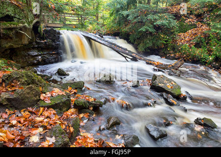 Autumn leaves are strewn along riverbanks and on rocks as Upper Chapel Falls cascades downriver at Pictured Rocks National Lakes Stock Photo