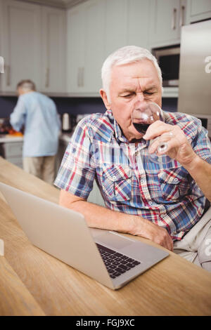 Senior man drinking red wine while using laptop Stock Photo
