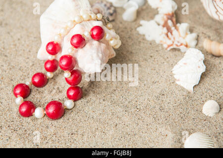 seashells and red necklace on sand at the beach Stock Photo