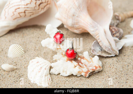 seashells and red earrings on sand at the beach Stock Photo