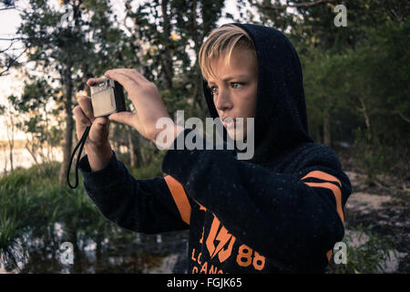 A boy taking a photo whilst on an adventure in the woods by the lake Stock Photo